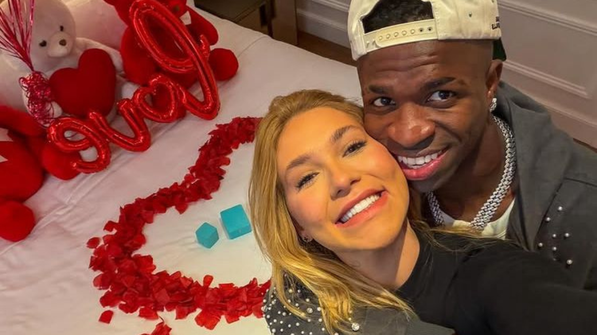 Vini Jr. Vinícius Júnior e Virginia estão abraçados à frente de uma cama com pétalas de rosa e balões vermelhos