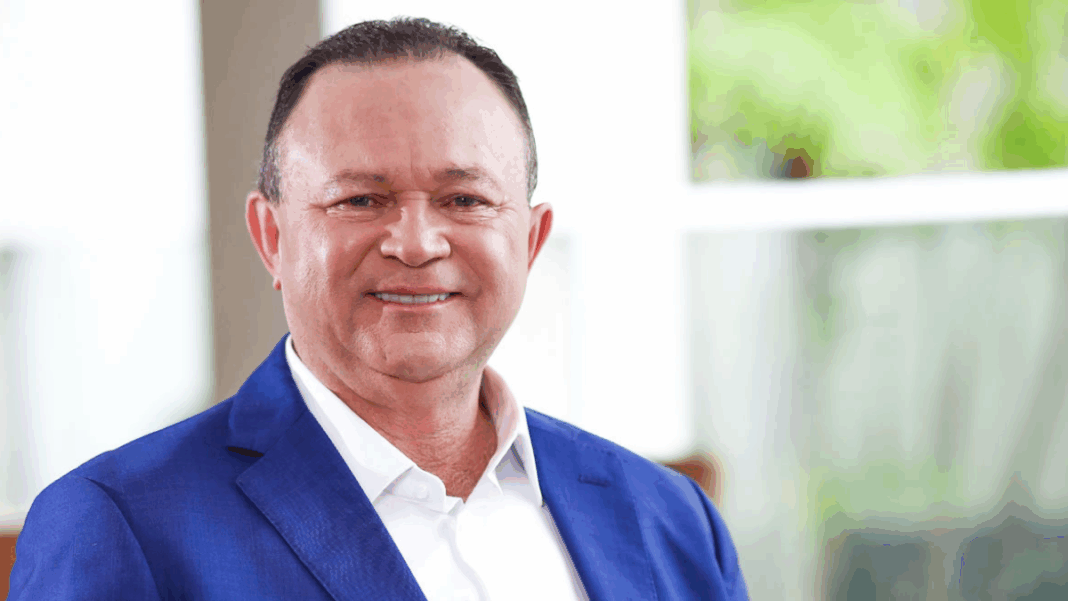 Carlos Brandão de roupa social, sorrindo e olhando para a câmera