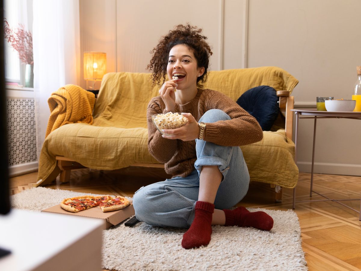 hbo-max Mulher assistindo televisão em uma sala com um pote de pipoca na mão.
