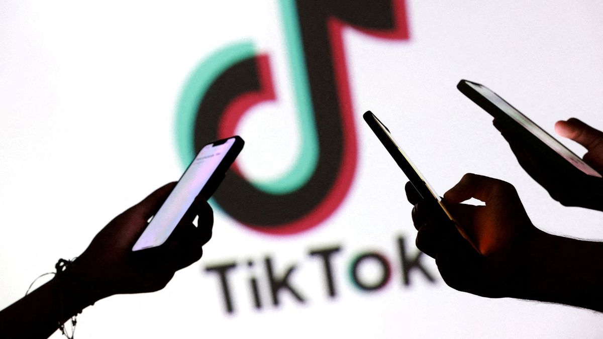 tiktok ok REUTERS Dado Ruvic Imagem mostra as mãos de três pessoas mexendo no celular, em primeiro plano. No segundo plano, há o logo da empresa TikTok.