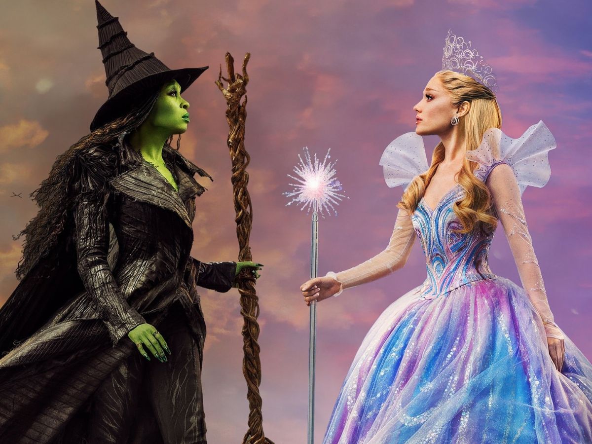 wicked-parte-2 Duas mulheres se encaram em um fundo de céu roxo. Uma mulher segura uma vassoura e é verde. A outra é branca e segura uma varinha.