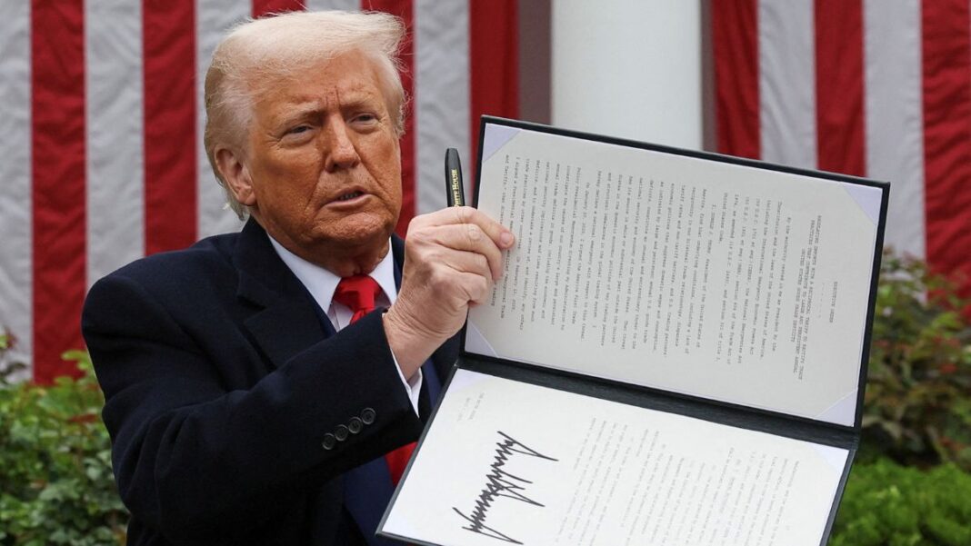 Donald Trump segura uma caneta com a mão direita e ergue texto de lei que assinou