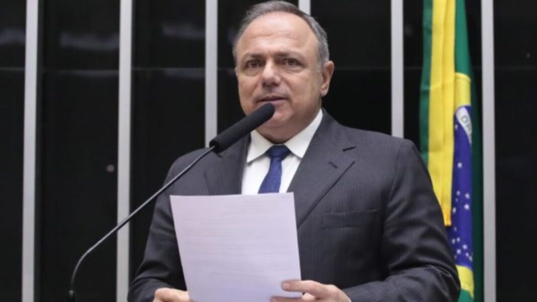A foto é um retrato em plano médio-fechado de Eduardo Pazuello, ex-Ministro da Saúde e atualmente deputado federal, no plenário da Câmara dos Deputados.